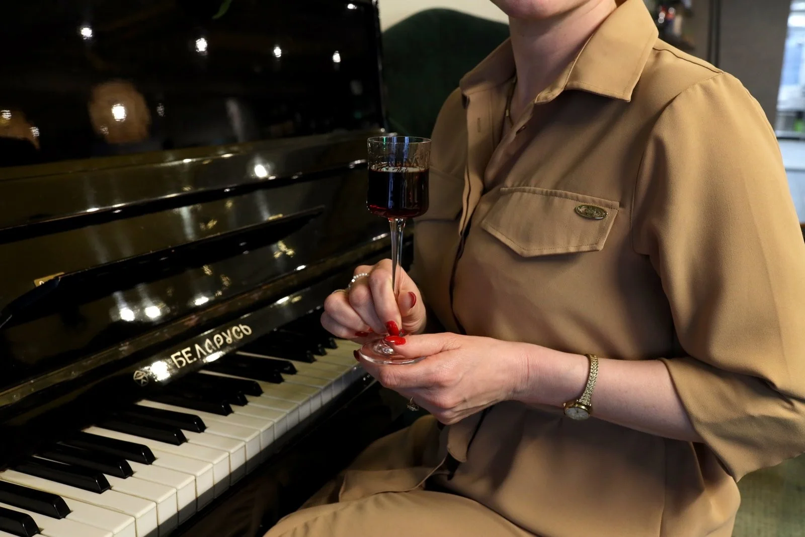 Klavir sa natpisom "БЕЛАРУСЬ". Osoba drži čašu vina, sjedeći pored klavira.