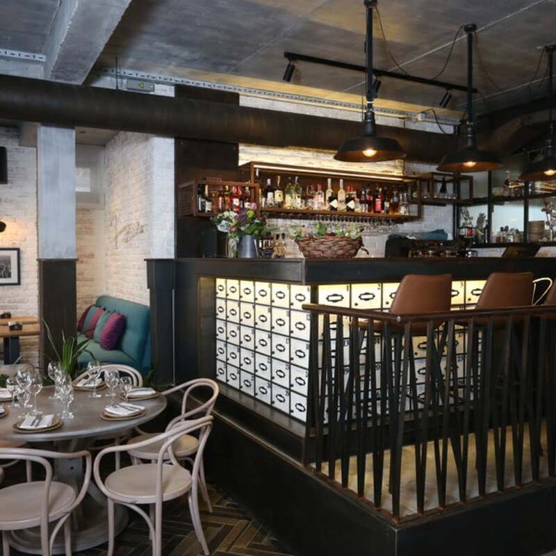 Stolice i sto s tanjirima stoje ispred ugostiteljskog šanka u modernom restoranu. Na šanku su izložene boce pića.